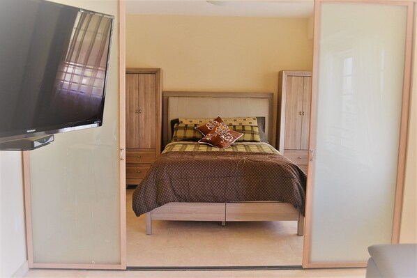 A bedroom with a bed, a television, and wooden wardrobes.