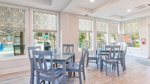 Un espace repas comprenant plusieurs tables et chaises, de grandes fenêtres ornées de motifs décoratifs et une vue sur une piscine extérieure.
