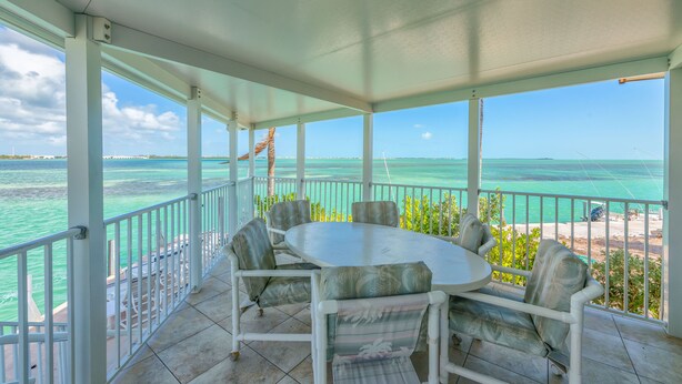 A covered outdoor area with a round table and chairs, overlooking a beach and turquoise waters. - Dock, Htd 80' Pool, Deep Channel, 15 Min To Key West  (Cudjoe Key)