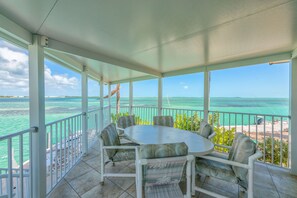 A covered outdoor area with a round table and chairs, overlooking a beach and turquoise waters. - Dock, Htd 80' Pool, Deep Channel, 15 Min To Key West  (Cudjoe Key)
