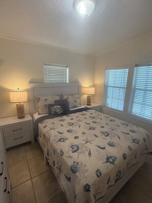 A bedroom with a bed, two bedside lamps, a window with blinds, and a ceiling light.