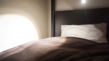 Ein Bett mit einem weißen Kopfkissen und einer braunen Decke in einem Zimmer, das ein dunkles Kopfteil und eine Lichtquelle darüber hat.