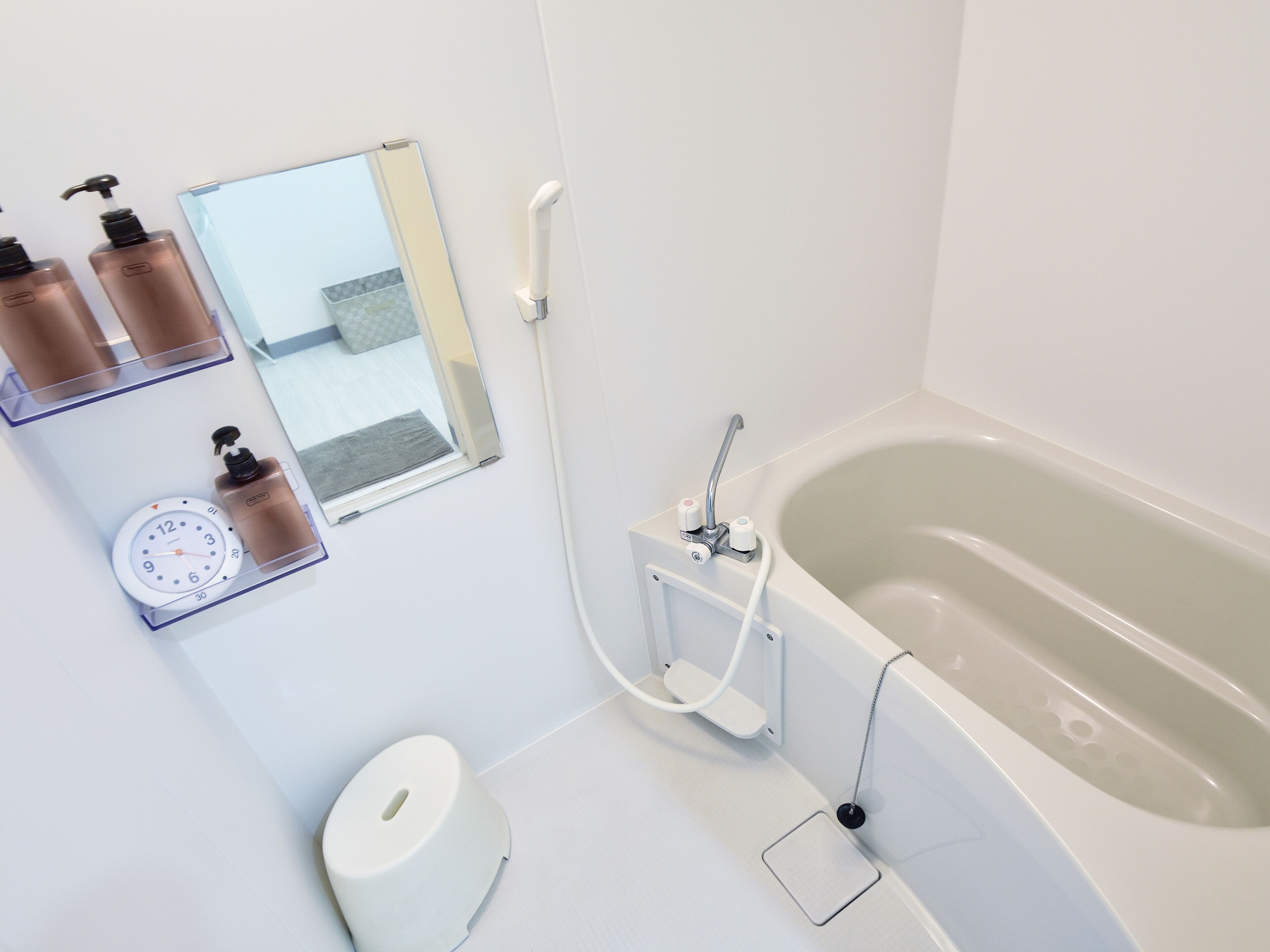 A modern bathroom with a bathtub, a mirror, a clock, and toiletries on a shelf.
