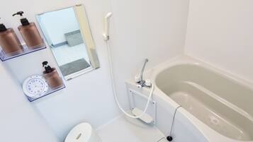 A modern bathroom with a bathtub, a mirror, a clock, and toiletries on a shelf.