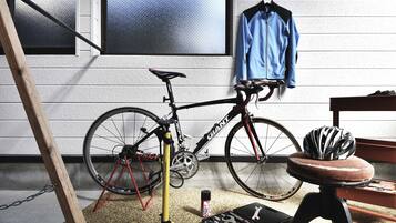 Una bicicleta con un kit de herramientas y un casco sobre un piso alfombrado, una chaqueta azul colgada y una escalera de madera.