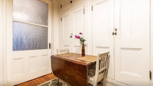 A room with a wooden table, chairs, a vase with flowers, and white doors with a frosted glass window. - Elegant 3 Bed Apt ★ ★ ★ ★ ★ Mins to Manhattan (Hoboken)