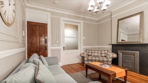 A living room with a sofa, a plaid armchair, a wooden coffee table, a fireplace, and a large mirror on the wall. - Elegant 3 Bed Apt ★ ★ ★ ★ ★ Mins to Manhattan (Hoboken)