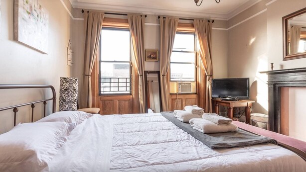 A hotel room with a large bed, a television, a fireplace, and a window with curtains. - Elegant 3 Bed Apt ★ ★ ★ ★ ★ Mins to Manhattan (Hoboken)