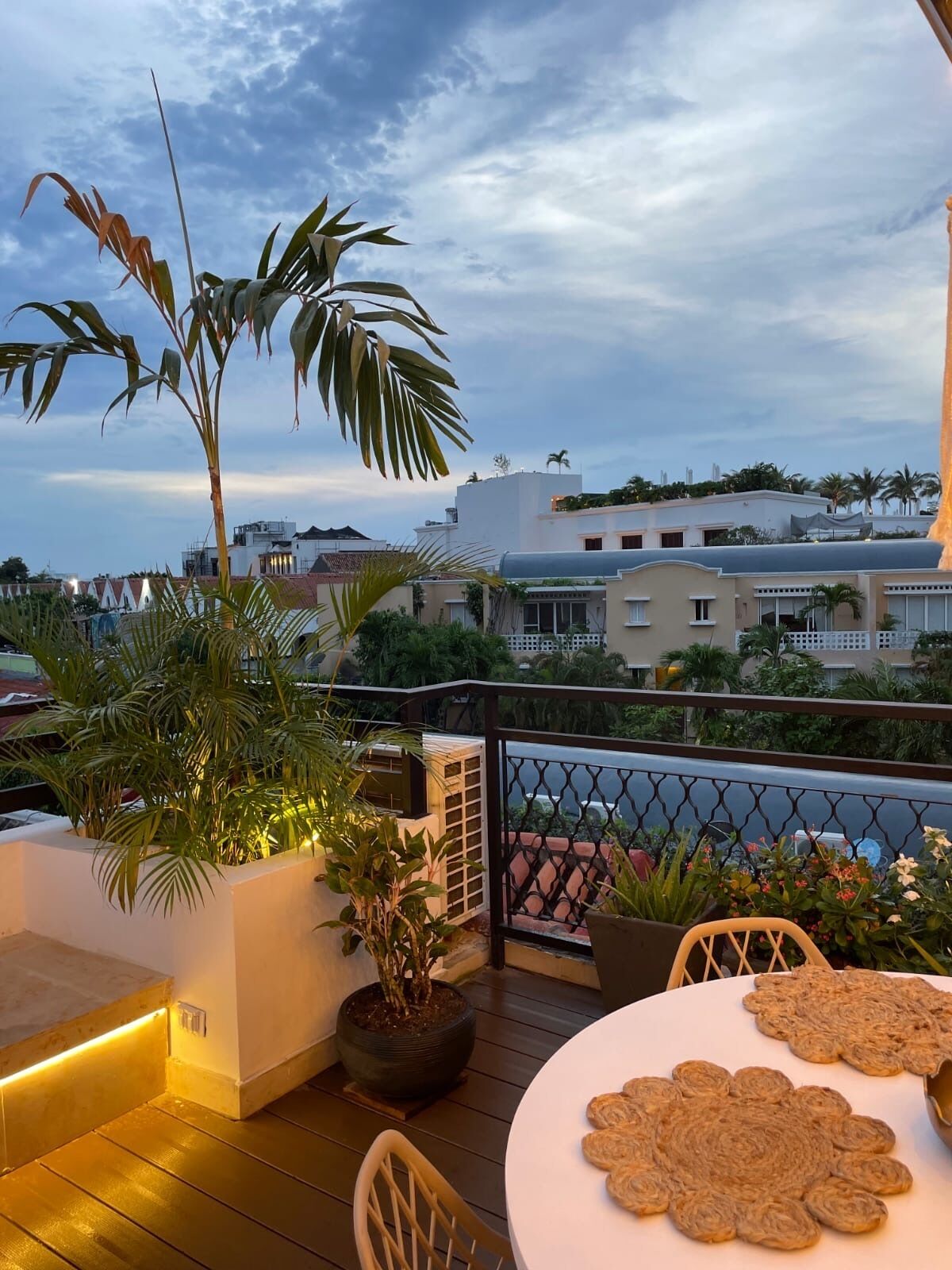 A balcony with a table, chairs, potted plants, and a view of buildings in the background.