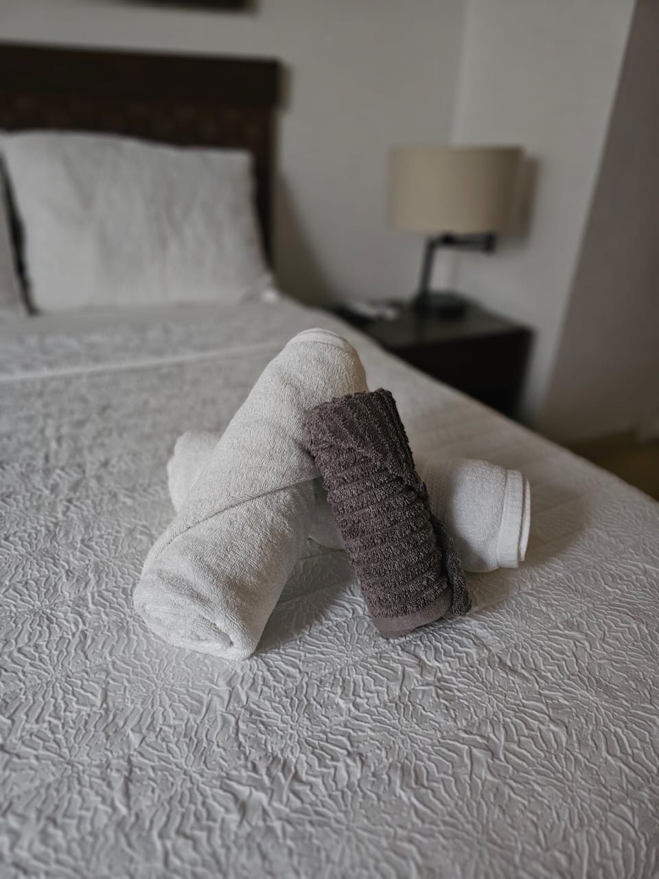 Een keurig opgemaakt bed met witte lakens en een opgevouwen paarse handdoek.