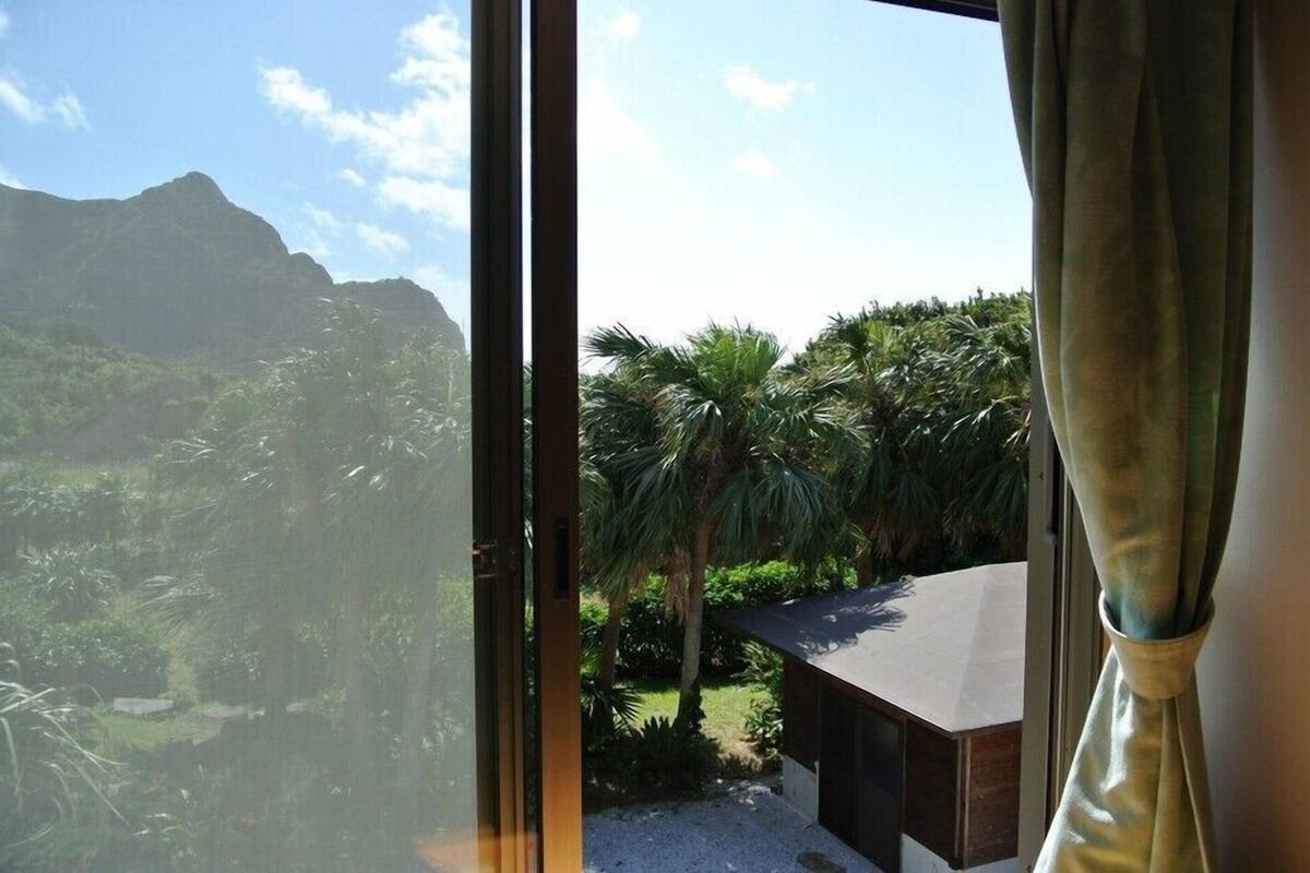 A view through a window of a room with a view of a mountainous landscape and palm trees.
