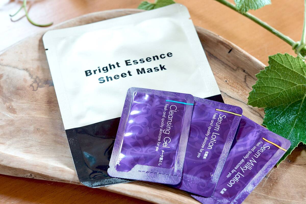 A tray with a Bright Essence Sheet Mask, a white bag, and three purple serum lotion packets.