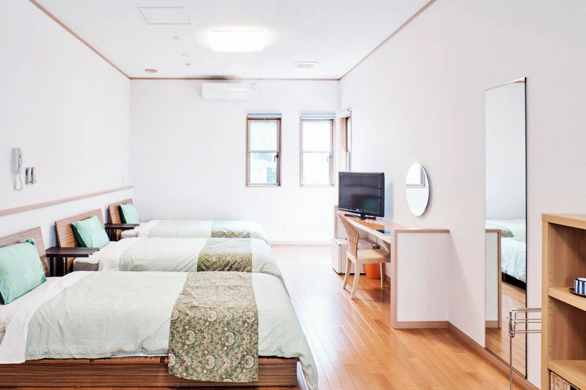 A hotel room with two beds, a desk with a computer, a TV, and a mirror.