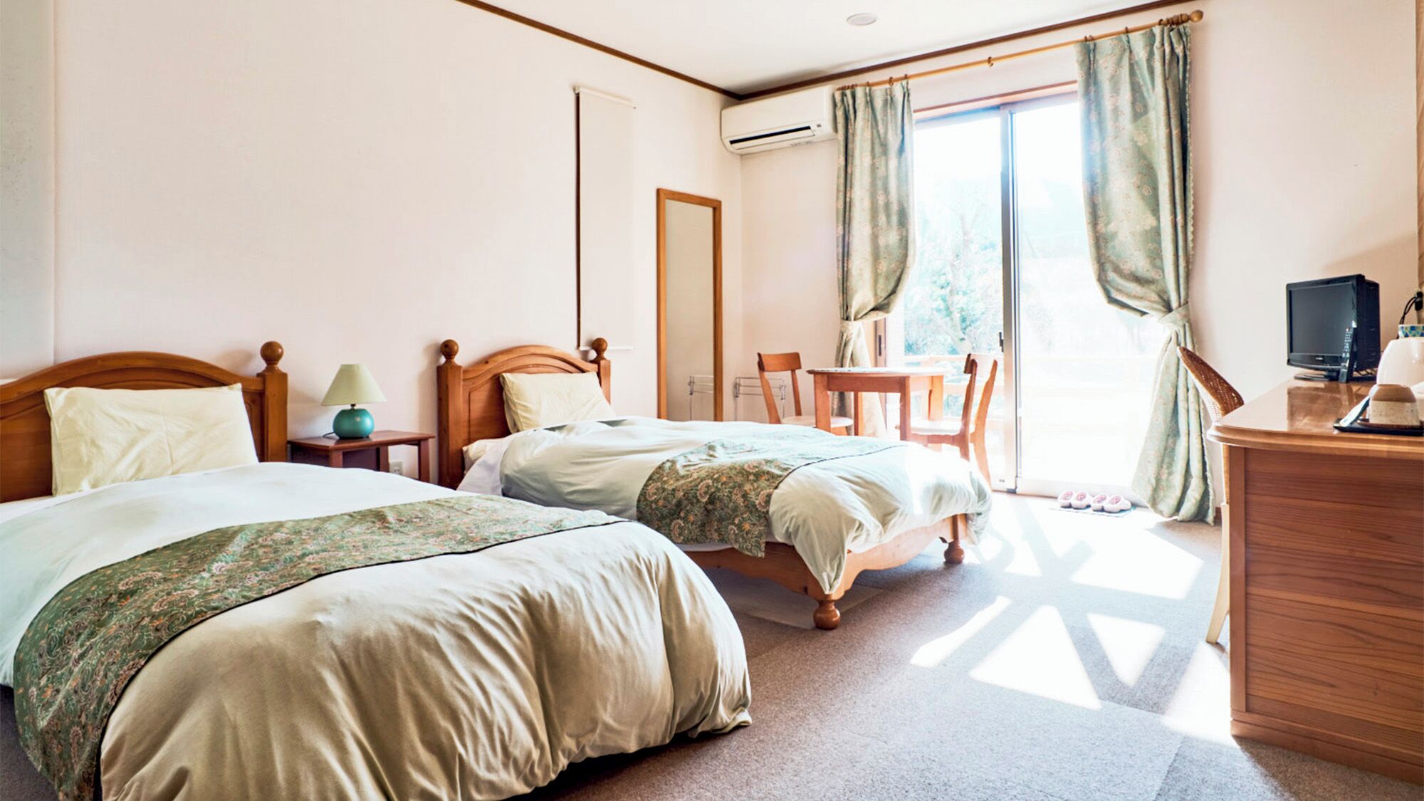 Ein Hotelzimmer mit zwei Betten, einem Schreibtisch mit Computer, einem Stuhl und Blick ins Freie.