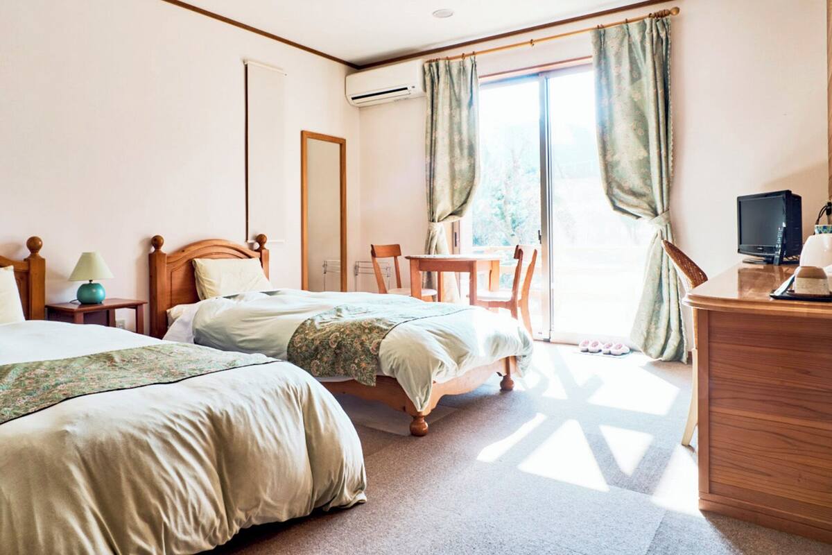 A hotel room with two beds, a desk with a computer, a chair, and a view of the outdoors.