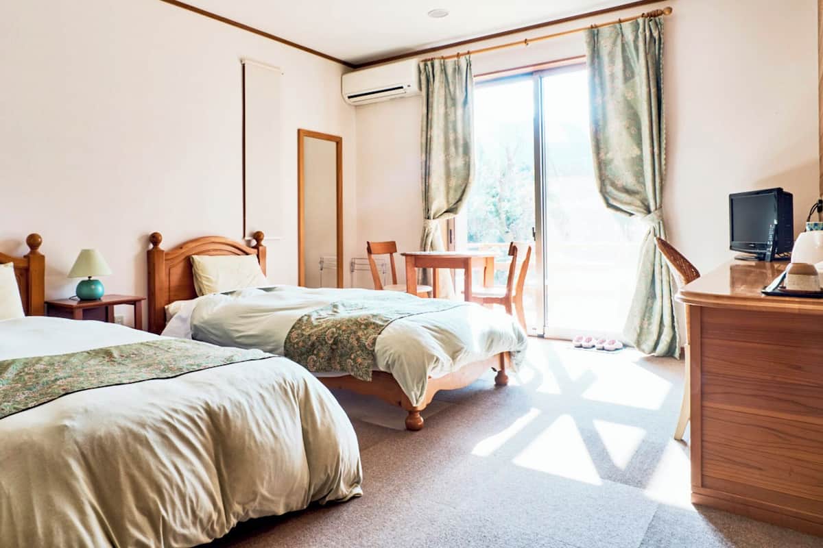 A hotel room with two beds, a desk with a computer, a chair, and a view of the outdoors.