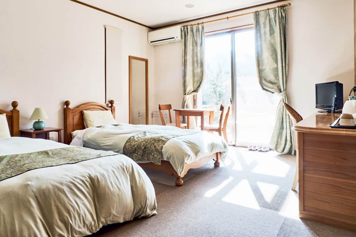 A hotel room with two beds, a desk with a computer, a chair, and a view of the outdoors.