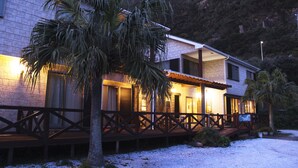 A two-story building with a balcony, palm trees, and a mountainous backdrop. - Mantenbo (Hachijo)