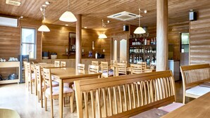 A spacious wooden dining area with high ceilings and pendant lighting, featuring a long communal table and several benches. - Mantenbo (Hachijo)