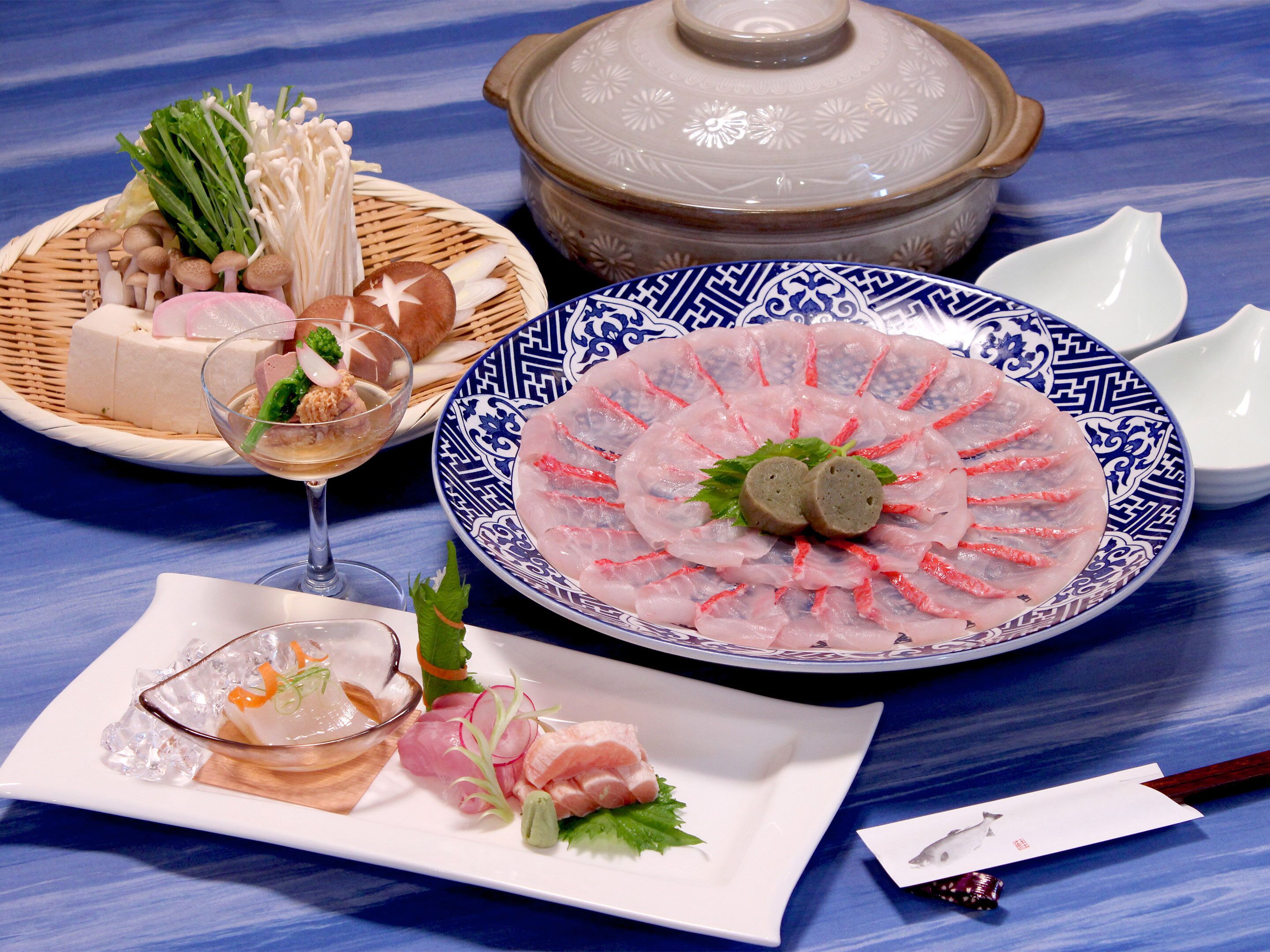 A table with various dishes, including sashimi, a glass of sake, and a ceramic pot.