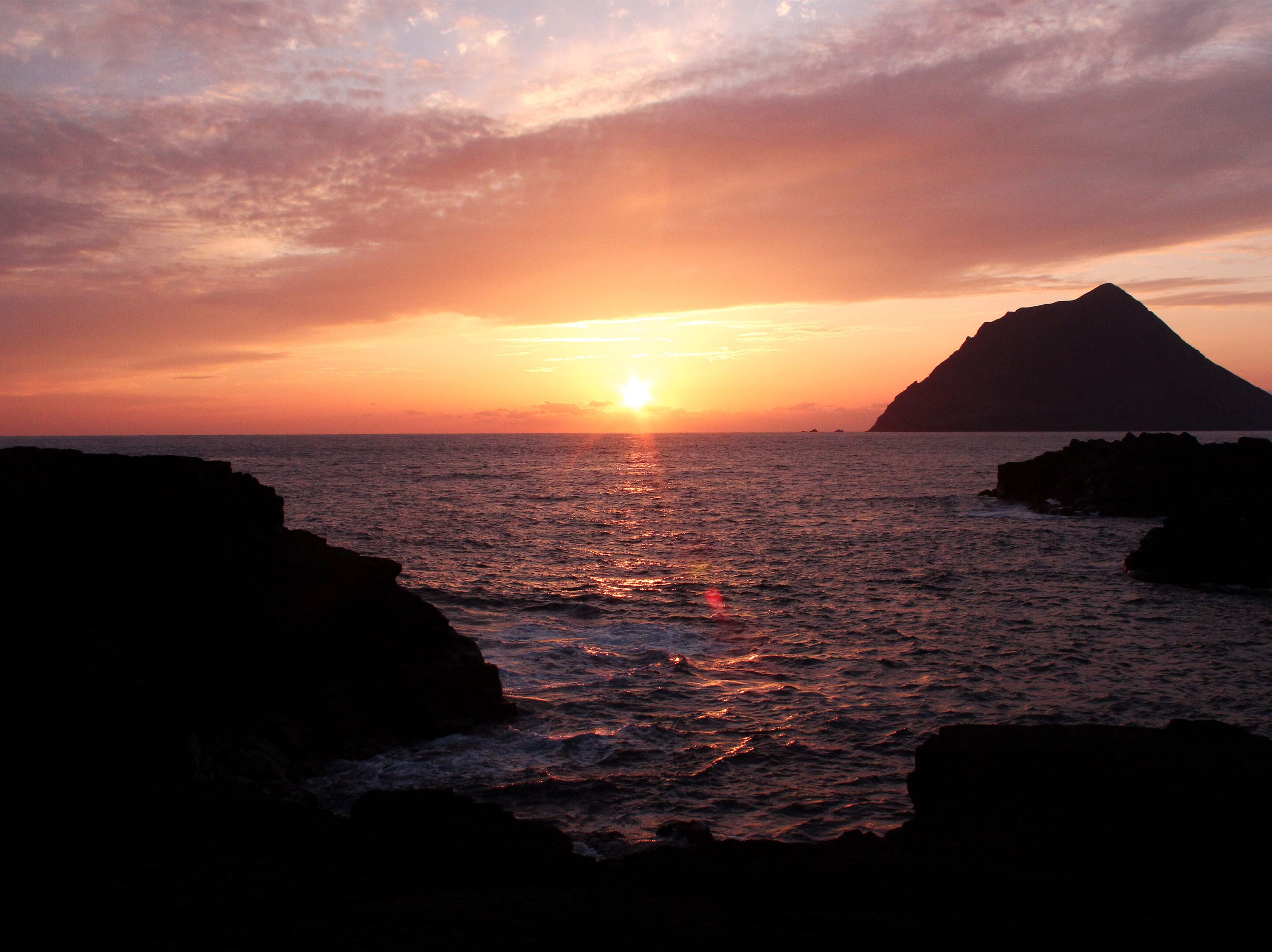 A sunset over a body of water with rocky formations.