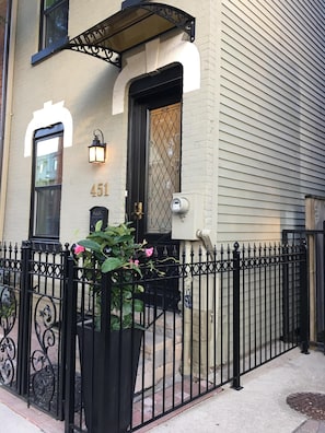 Classic architecture with a central entrance and symmetrical design, featuring a black iron fence and a potted plant.