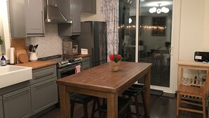 A modern kitchen with grey cabinets, a wooden table, and a sliding glass door leading to a dining area. - Beautiful 4Br downtown garden house. Sleeps 12 (Toronto)
