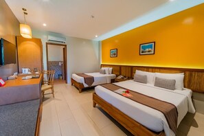 A hotel room with two beds, a desk, a chair, an air conditioning unit, and a wall-mounted TV. - Bohol Beach Club (Panglao)