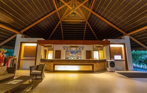 A reception area with a registration desk, information board, and a cashier. There is a wicker chair and a table in the foreground. - Bohol Beach Club (Panglao)