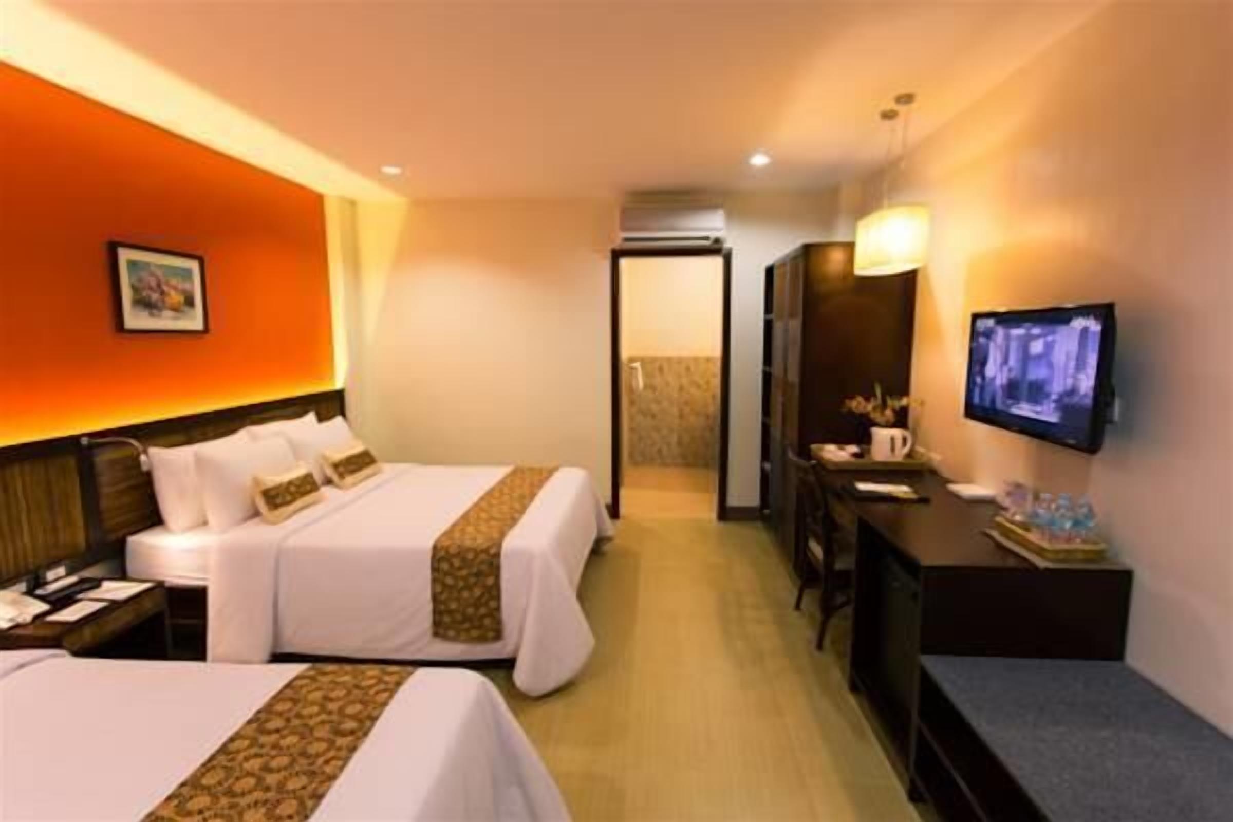 Habitación de hotel con dos camas, un escritorio, un televisor y un baño visible a través de una puerta abierta.