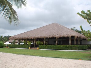 A thatched-roof building with a covered outdoor area, surrounded by well-maintained greenery and a sandy foreground. - Bohol Beach Club (Panglao)