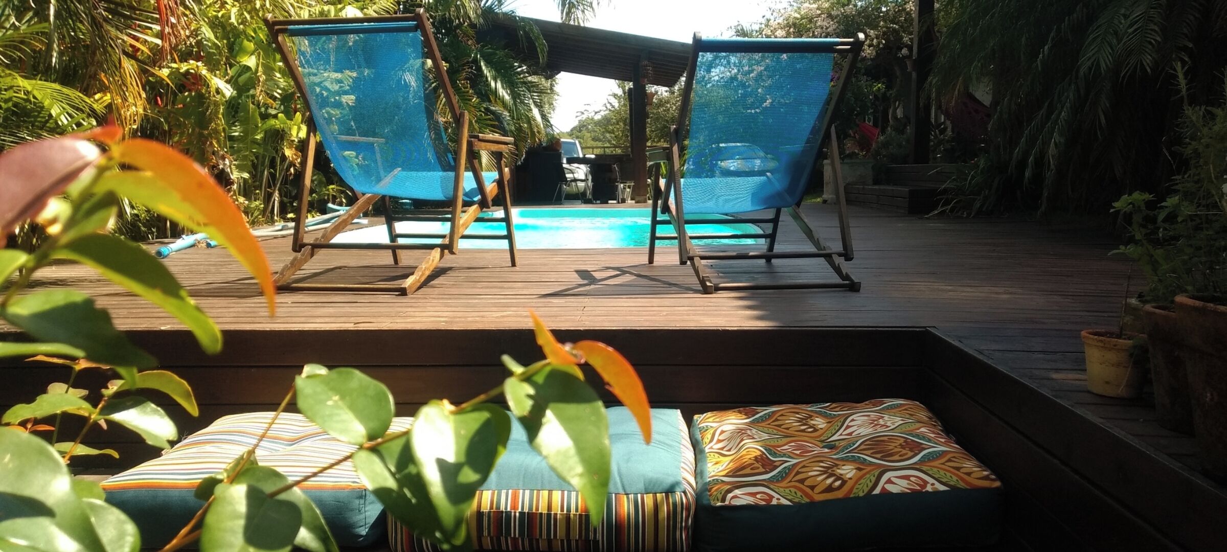 A wooden deck with two blue mesh chairs and a pool.