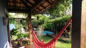 Una terraza de madera con una hamaca, piscina y abundante vegetación.