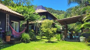 Una casa con porche, hamaca y patio rodeado de exuberante follaje y árboles.