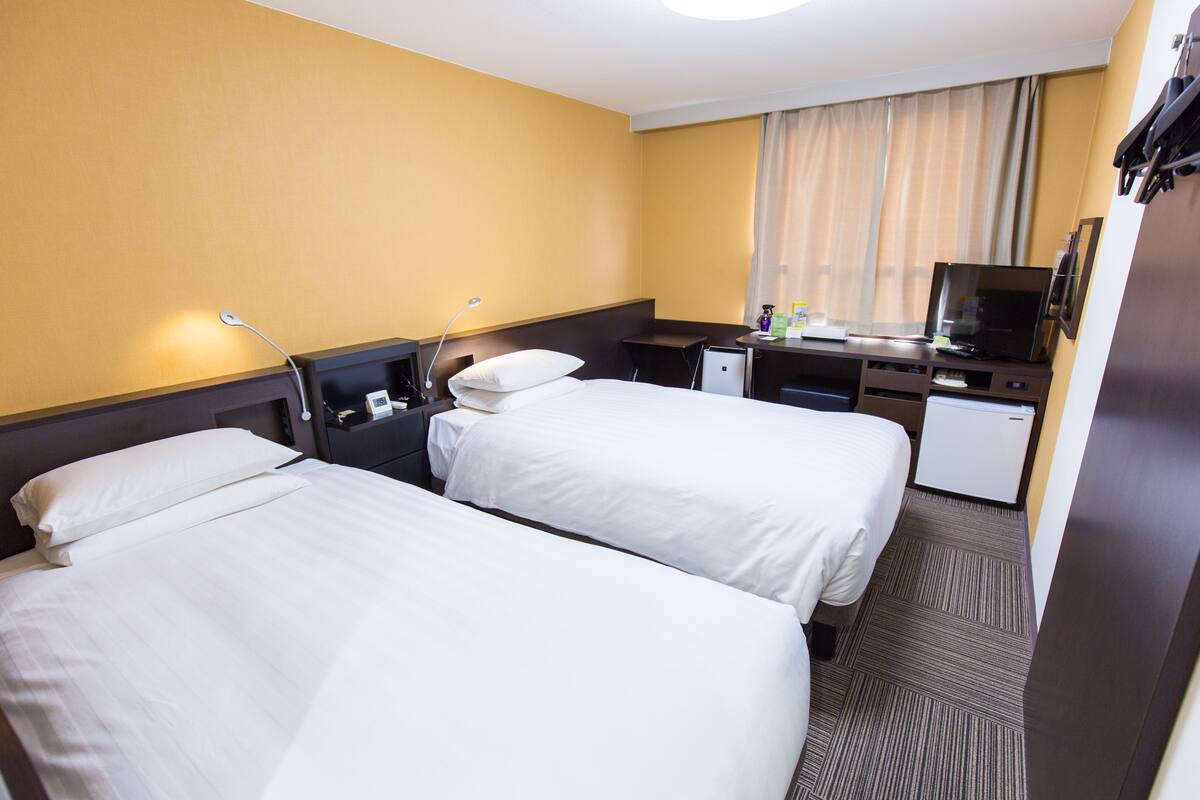 A hotel room with two beds, a desk, a television, and a small refrigerator.