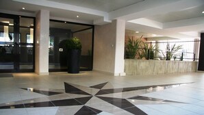 Una hall con pavimento in piastrelle geometriche, un'ampia pianta in vaso e vista sull'esterno tramite una porta in vetro.