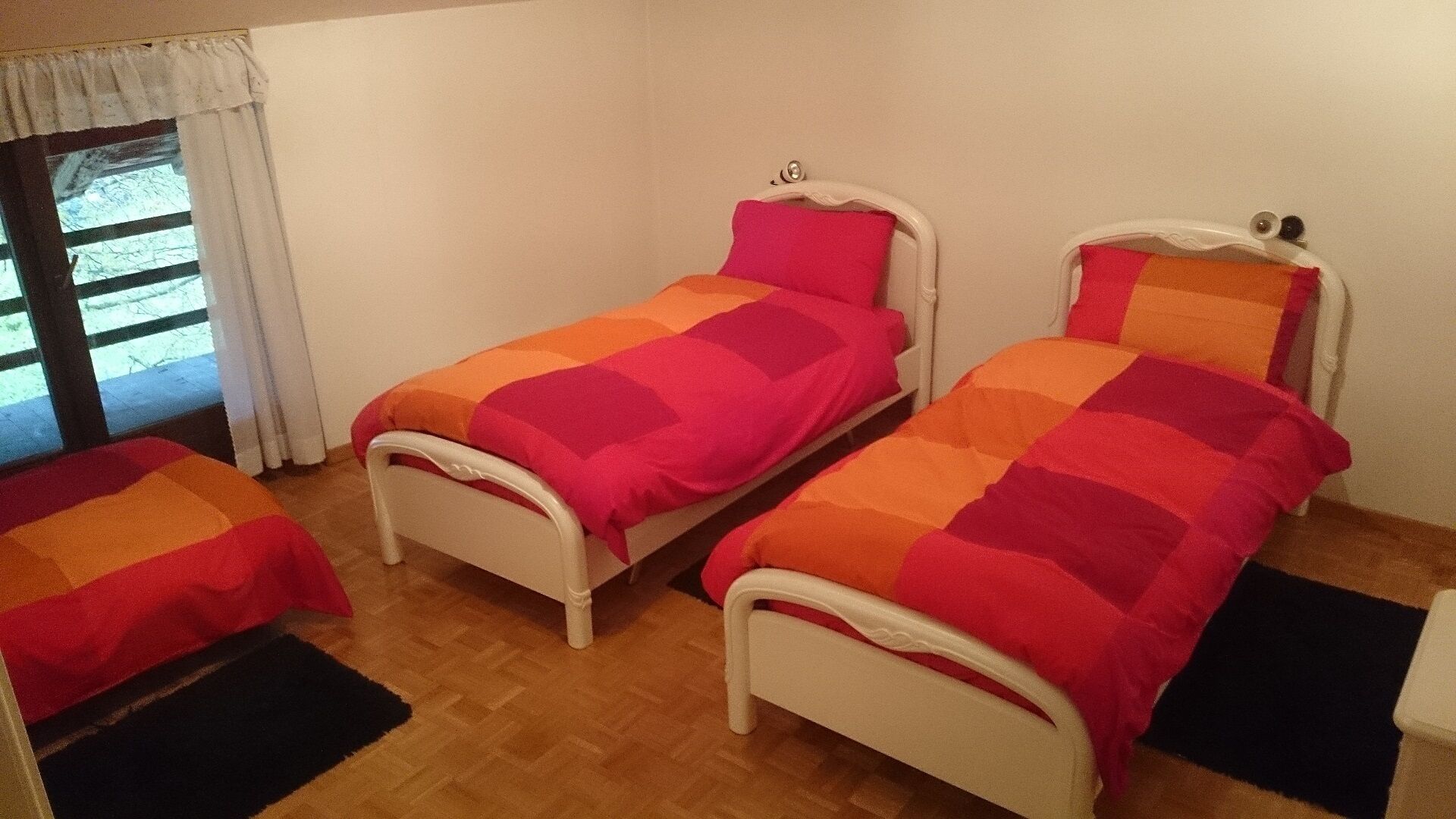 Una habitación con dos camas individuales, una ventana con cortinas y suelo de madera.