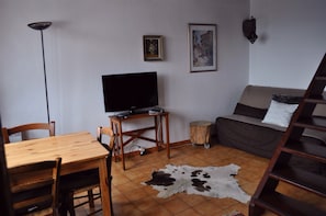 A living room with a wooden dining table, a sofa, a television, and a cowhide rug.