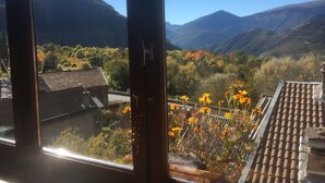 Vista desde una ventana con paisaje montañoso, follaje otoñal y un edificio con tejado de baldosas tradicionales.