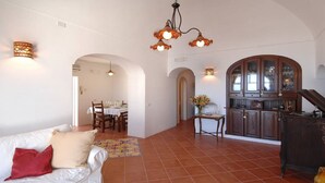 Amplia sala de estar con una mesa de comedor, una cocina con armarios de madera y un sofá blanco con un cojín rojo.