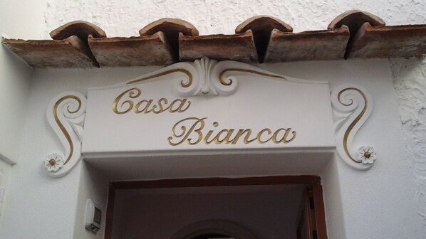 En skylt ovanför en dörröppning med texten ”Casa Bianca” och dekorativa element.