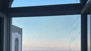 Vista a través de una ventana con cielo despejado, un edificio con torre de reloj y un horizonte lejano.