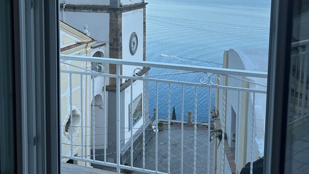 Un balcón con vistas al mar y un edificio blanco con un reloj.