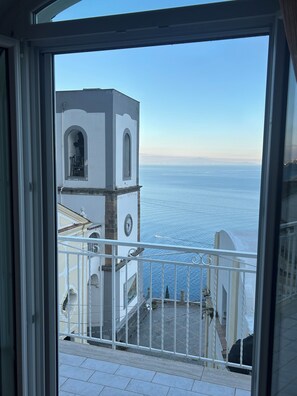 A balcony with a view of the sea and a white building with a clock.