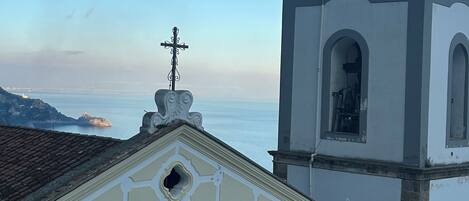 A building with a bell tower and a cross on top, overlooking a body of water.