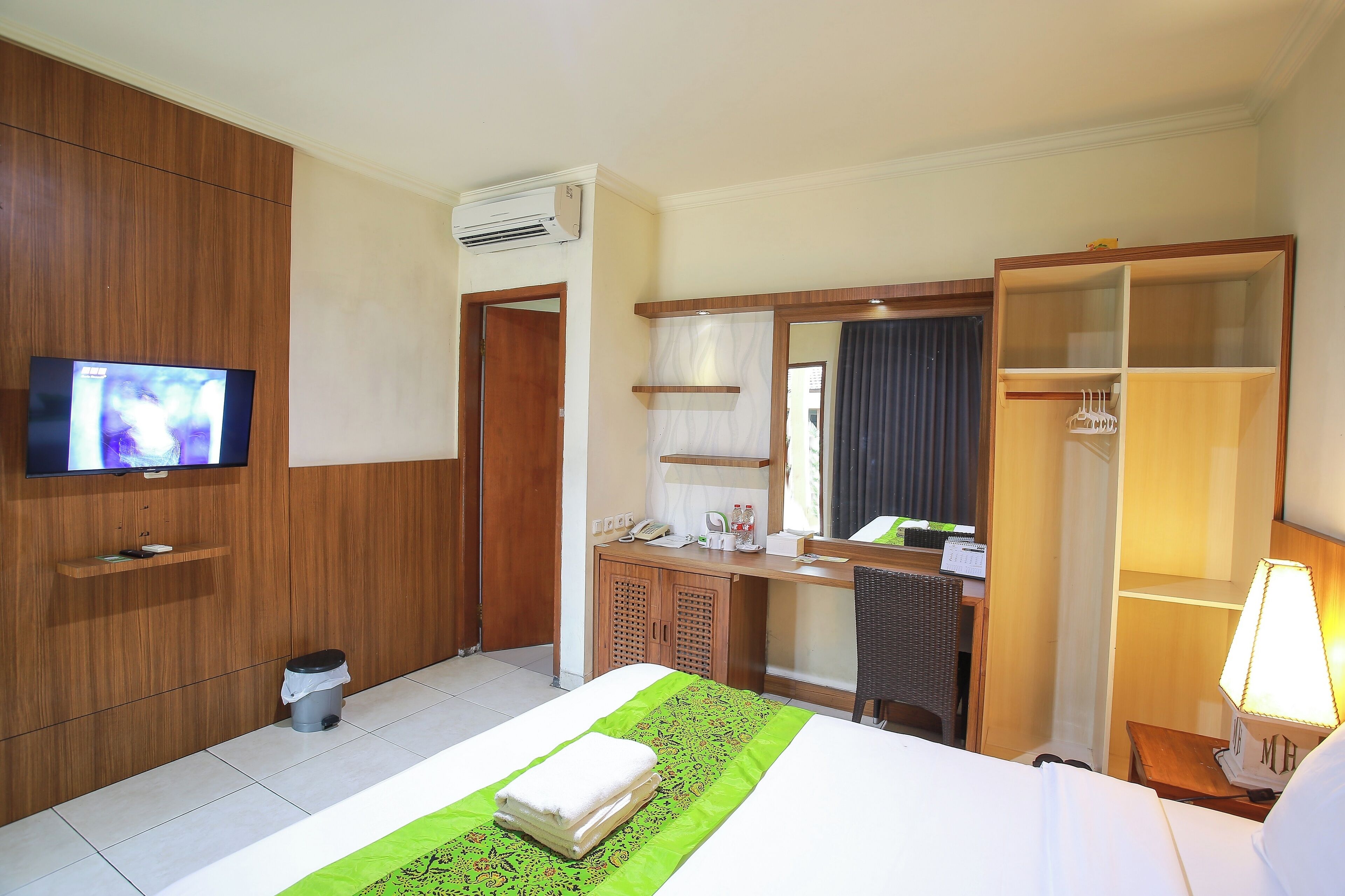 A hotel room with a bed, a TV, a desk, a wardrobe, and a mirror.