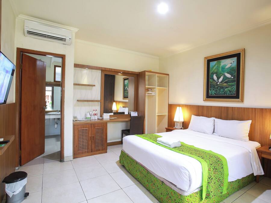 Habitación de hotel con cama, escritorio, espejo, televisión y un cuadro en la pared.