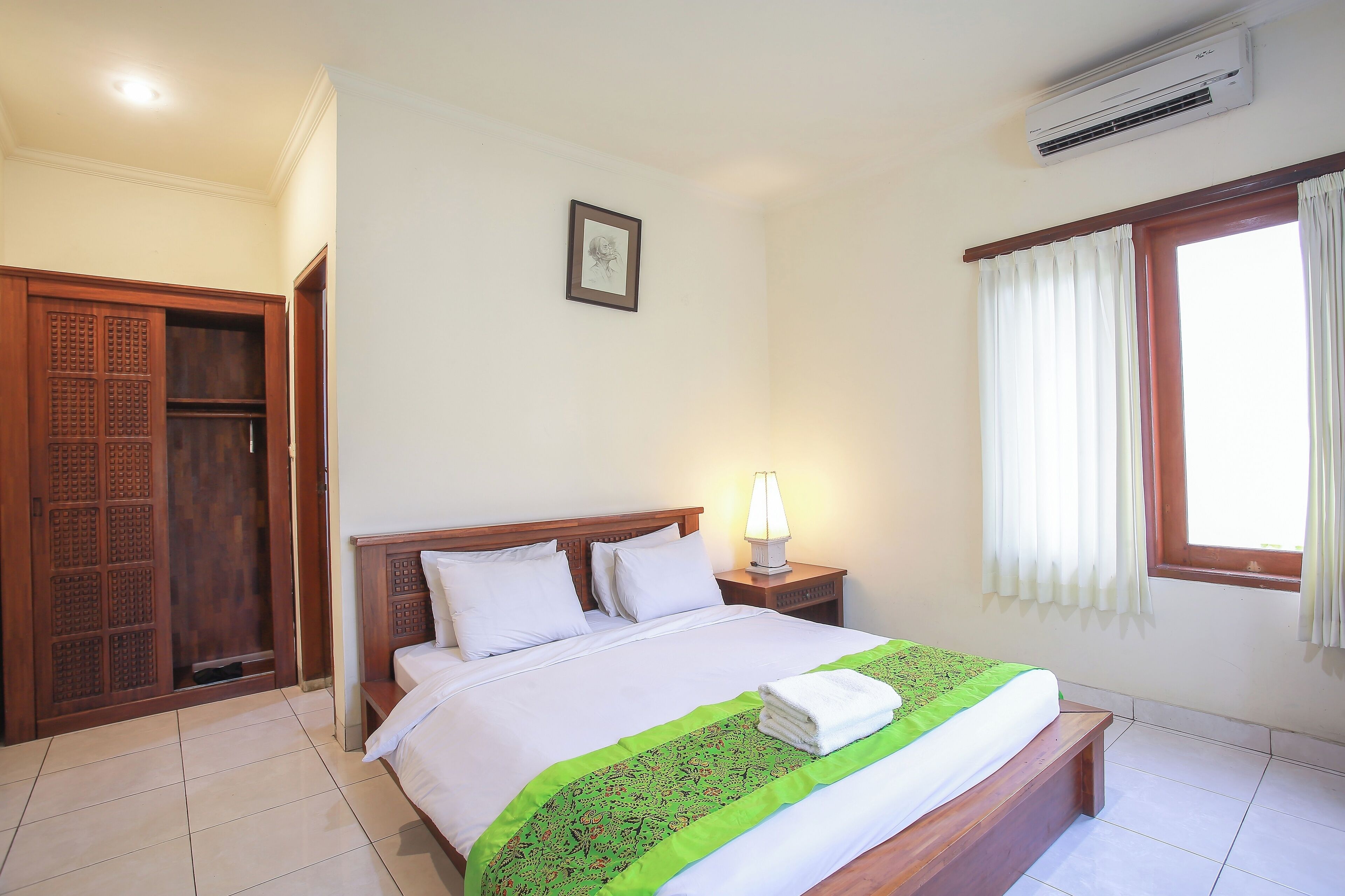 A neatly made bed with a green and white bedspread, a bedside lamp, and a window with curtains.