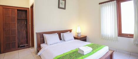 A neatly made bed with a green and white bedspread, a bedside lamp, and a window with curtains.