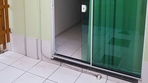 A room with a sliding glass door leading to a bathroom, a small shelf with toiletries, and a wooden chair outside. - Residencial Floripamar I (Florianópolis)